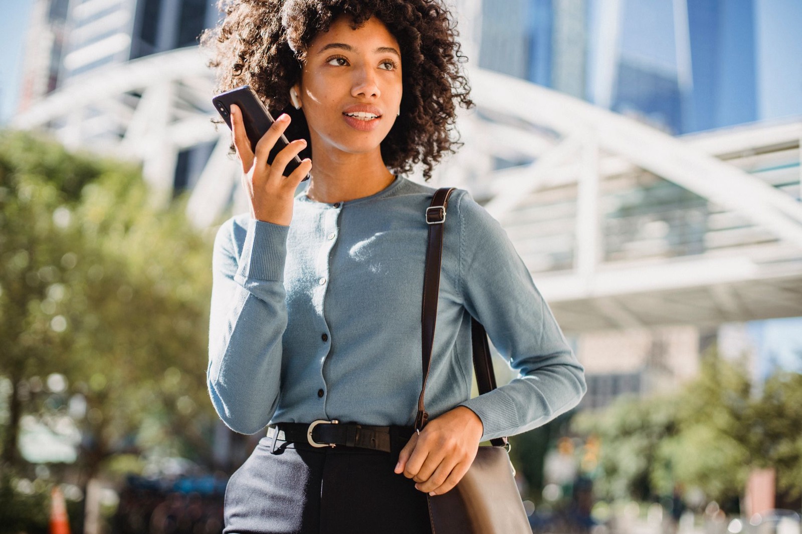 A person speaking English on their phone outdoors, smiling